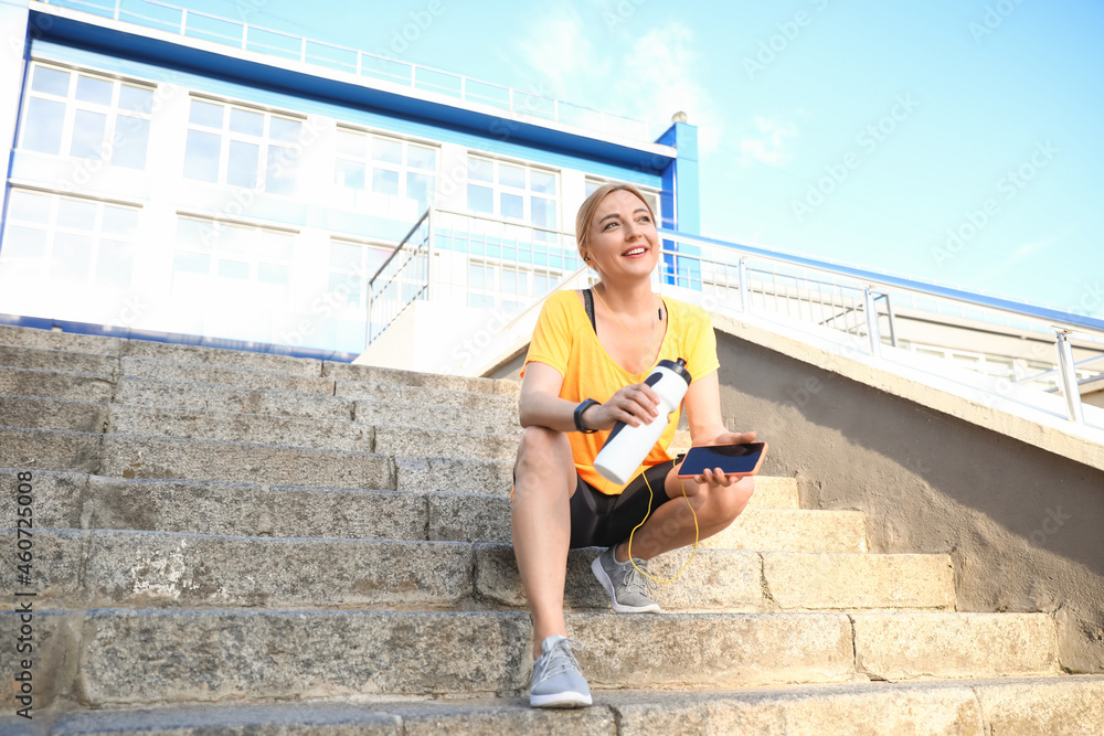 Sporty mature woman with bottle of water listening to music outdoors