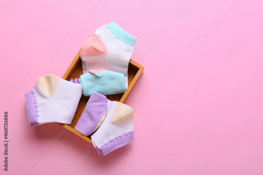 Wooden box with different socks on pink background