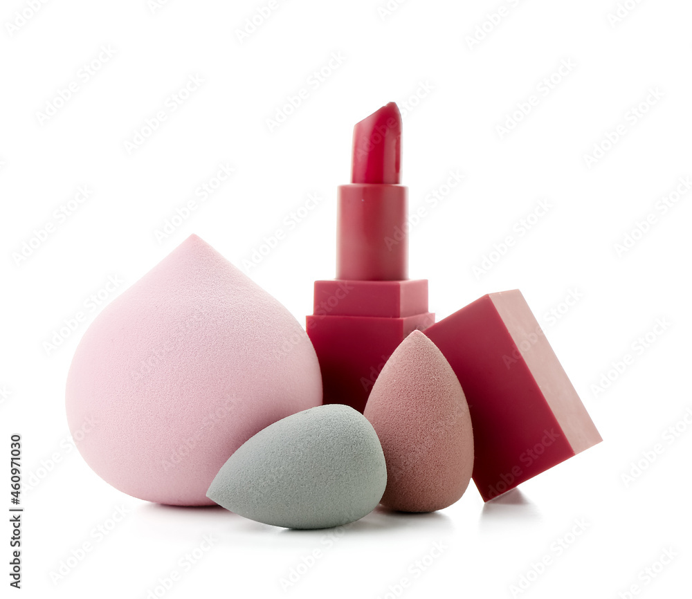 Stylish makeup sponges and lipstick on white background