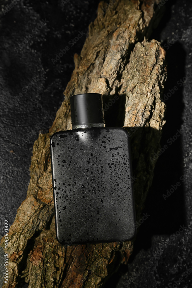 Perfume bottle covered with water drops on dark background