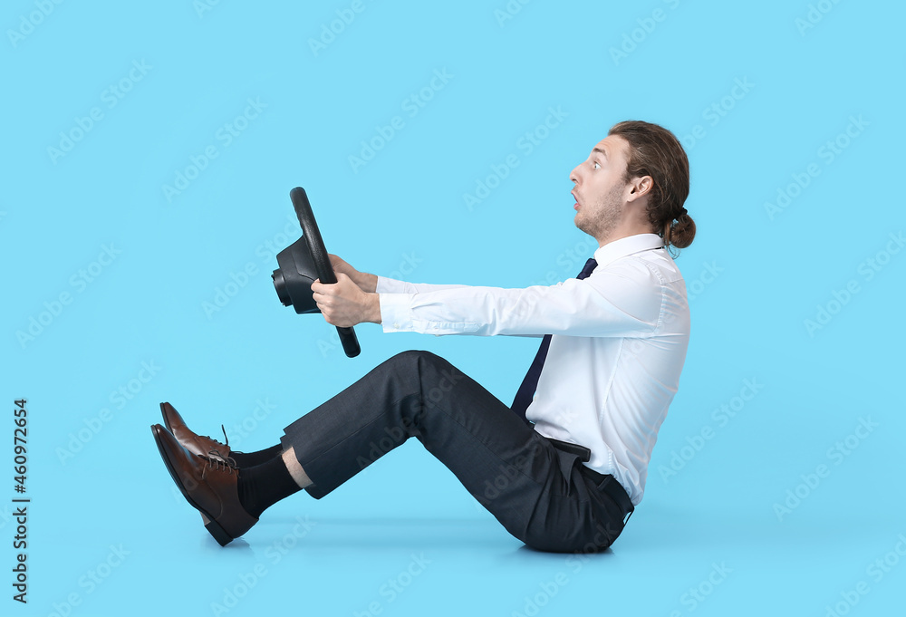 Shocked young man with steering wheel on color background