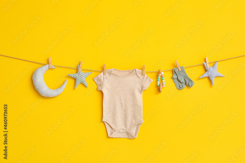 Baby bodysuit, socks and toys hanging on rope against color background