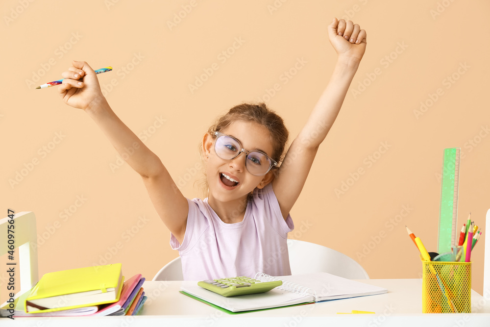 Little girl doing homework at table on color background