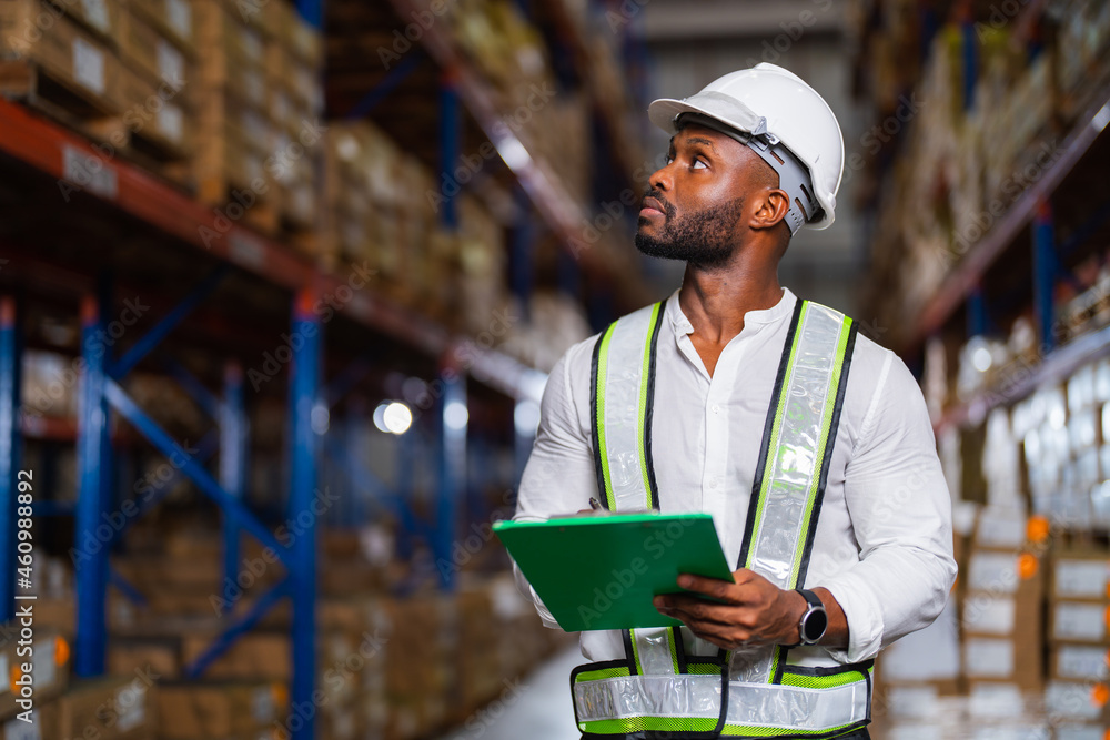 Portrait of an African warehouse manager holding a clipboard checking inventory in a large distribut