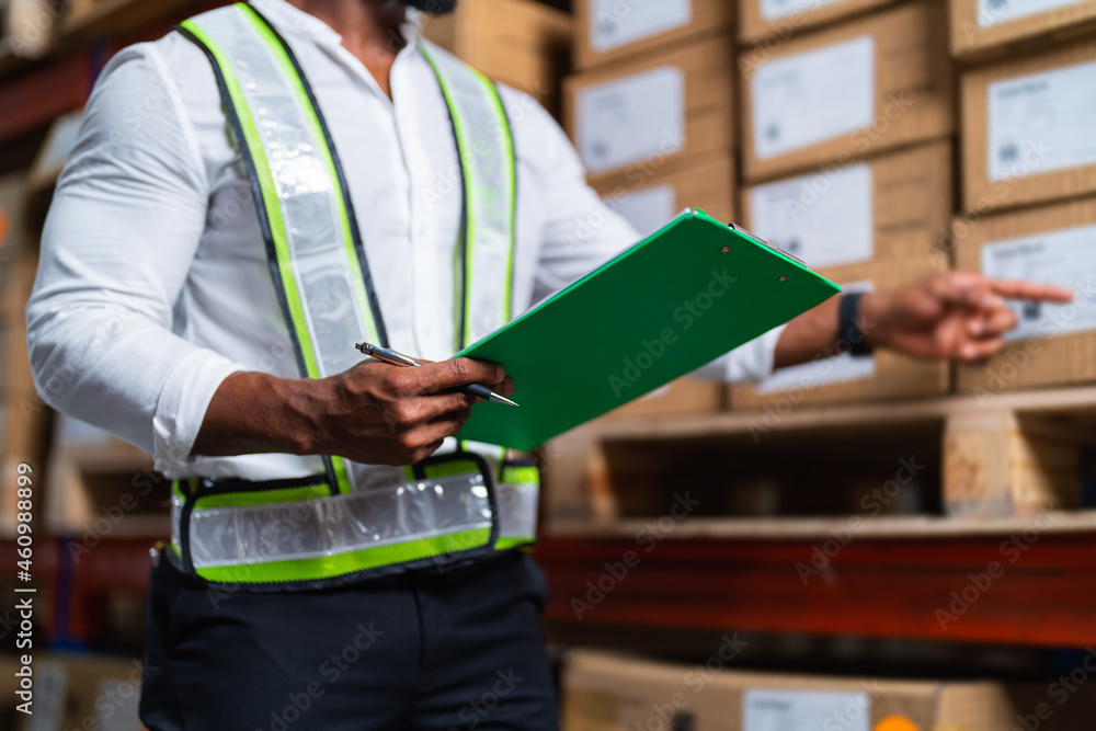 Portrait of an African warehouse manager holding a clipboard checking inventory in a large distribut