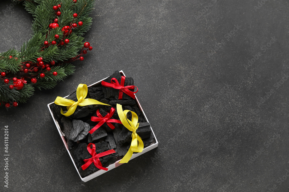 Box with coal and Christmas wreath on dark background