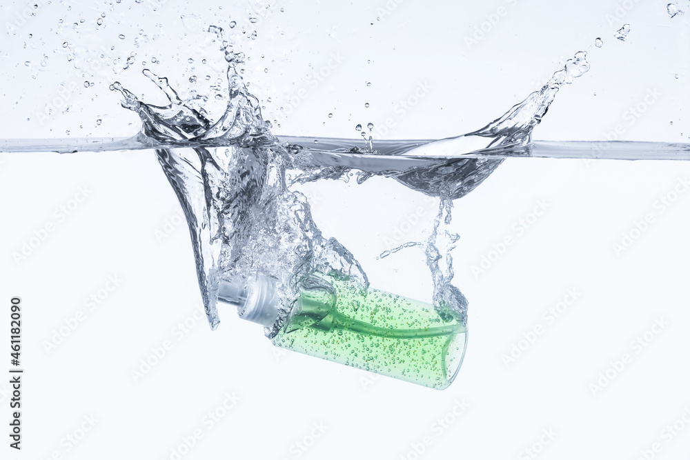 Bottle of cosmetic product in water with splashes on white background