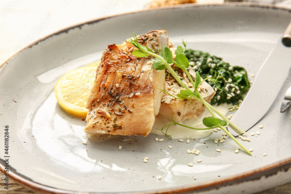 Plate with tasty baked cod fillet, pesto sauce and lemon on light wooden background, closeup