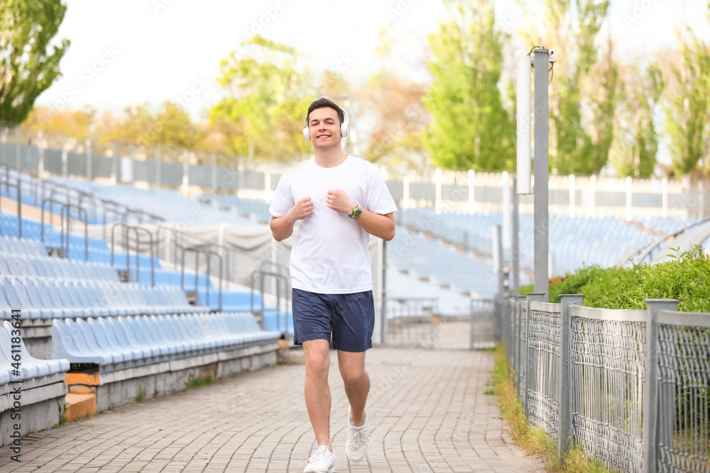 Sporty young man in headphones running at stadium