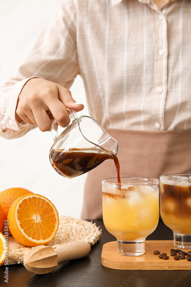 Woman pouring coffee into glass with orange juice on light background, closeup