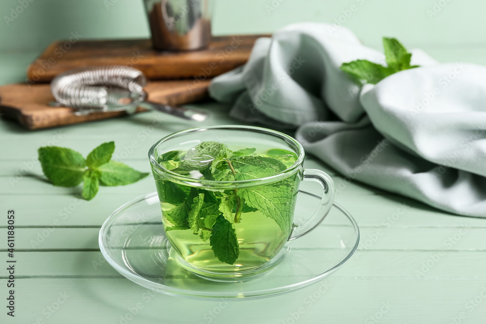 Glass cup of tasty mint tea on green wooden table