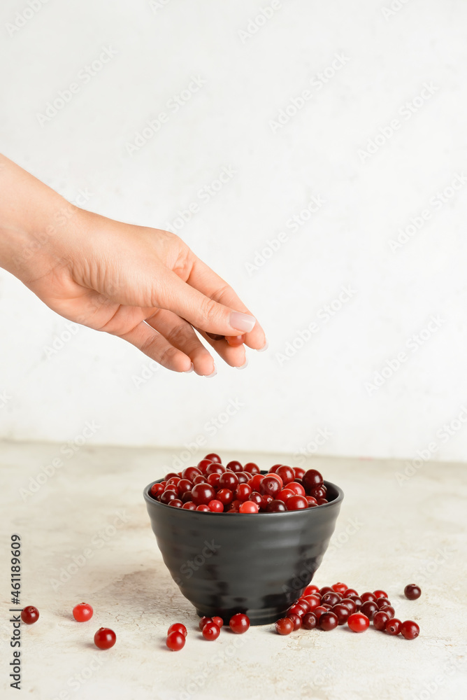 女性手和碗，浅色背景上有成熟的蔓越莓