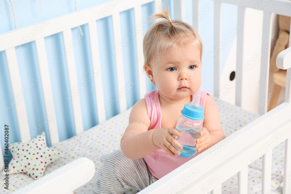 Cute baby girl with bottle of water in cot