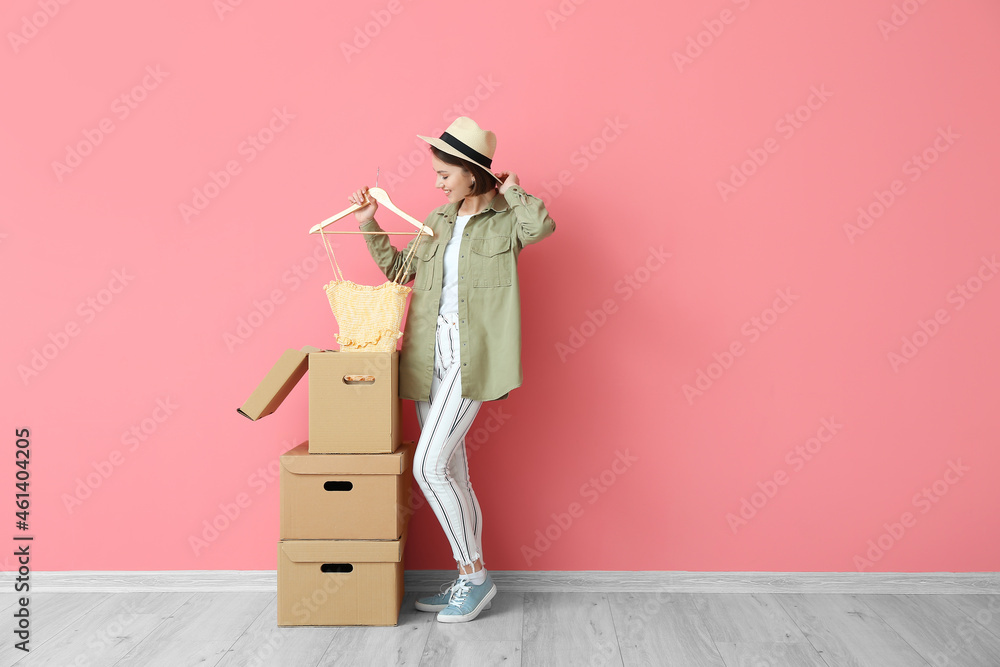 Young woman with wardrobe boxes and clothes near color wall