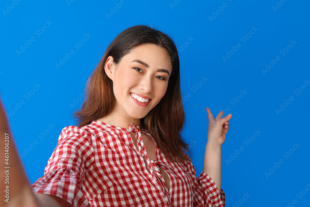 Stylish young Asian woman taking selfie on color background