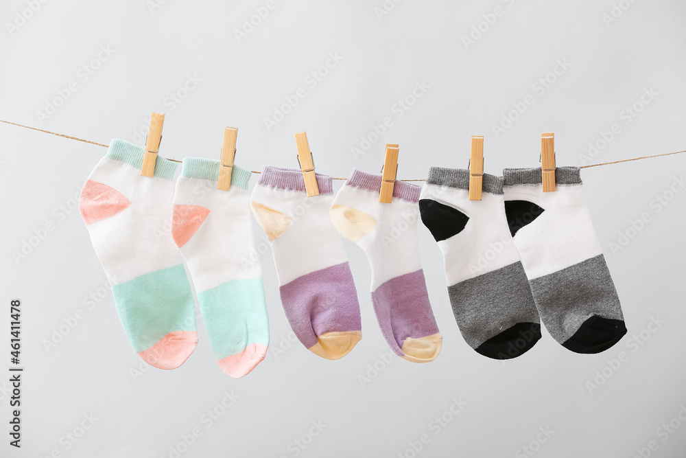 Different socks hanging on rope against grey background