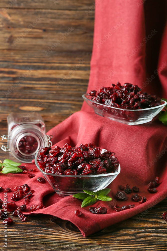 Bowls with tasty dried cranberries on wooden background