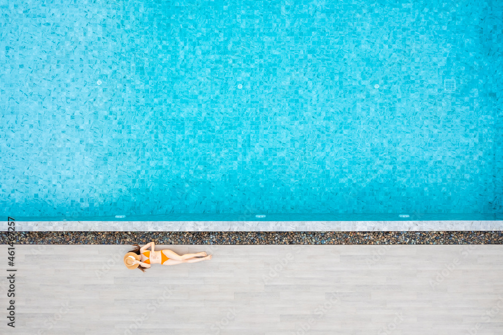 Top view of slim young woman in hat relaxing in resort swimming pool. Female enjoying sunbathing.