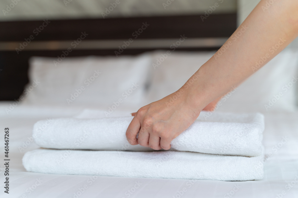 Closeup hands putting a stack of new clean bath towels on the bed. Hotel room service concept.