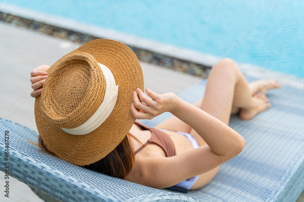 Rearview of woman in sun hat relaxing at luxury hotel tropical resort swimming pool. Female enjoying