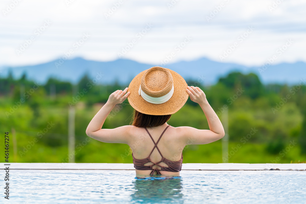 Rearview of woman in sun hat relaxing at luxury hotel tropical resort swimming pool. Female enjoying