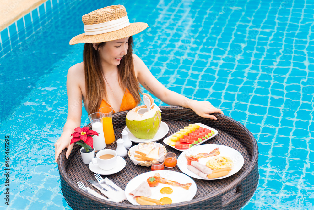 Portrait of Asian woman in swimwear enjoys floating breakfast tray in the luxury hotel resort. Femal