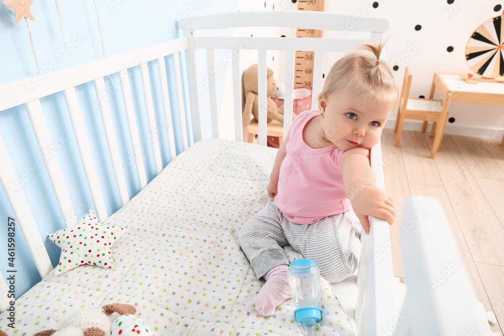 Cute baby girl with bottle of water in cot