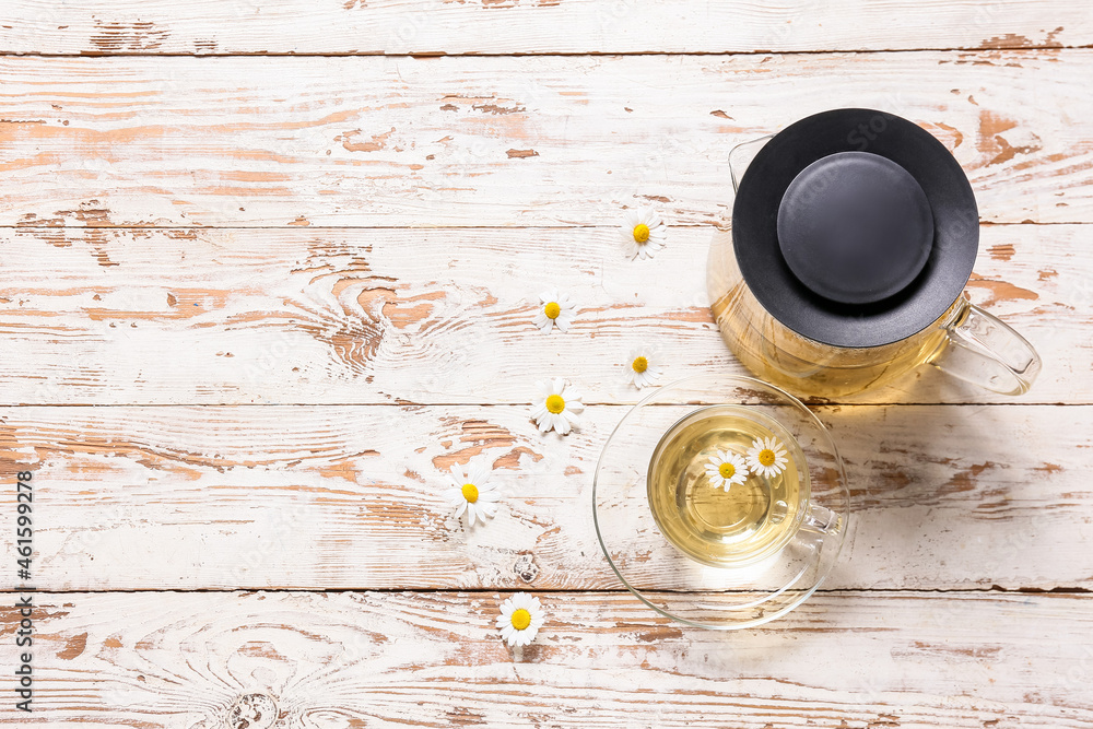 Teapot and cup of tasty chamomile tea on light wooden background