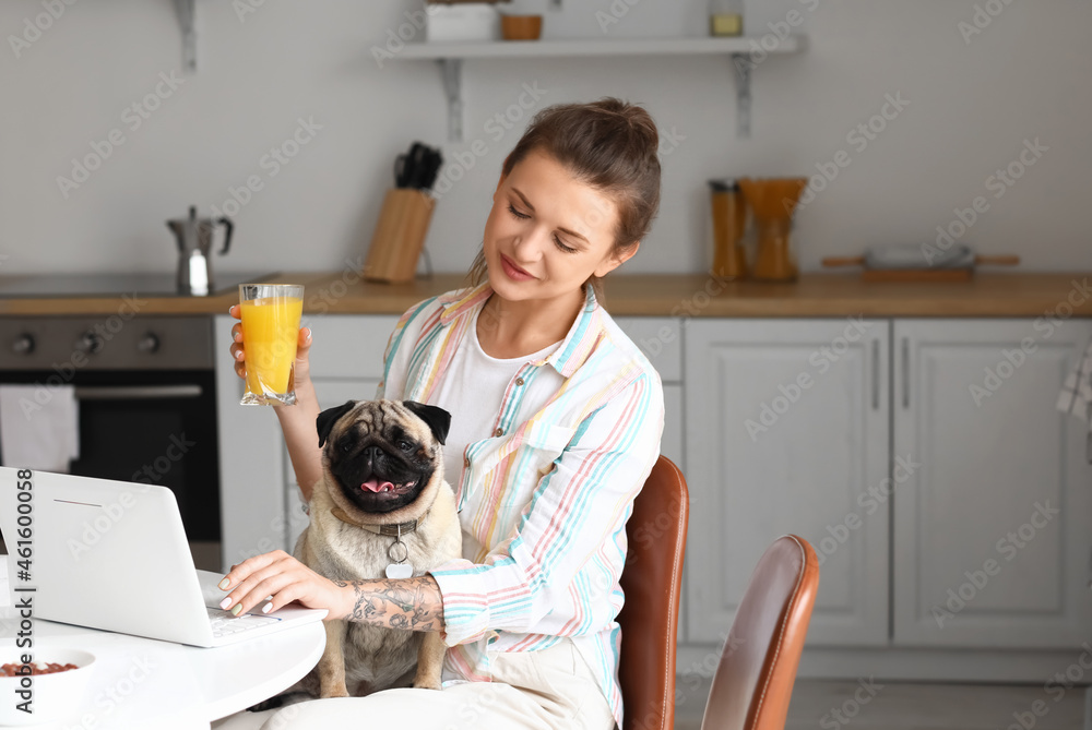 Young woman with cute pug dog drinking juice in kitchen