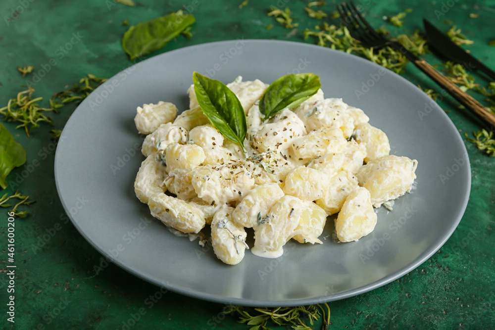 Plate of delicious gnocchi with creamy sauce on green background