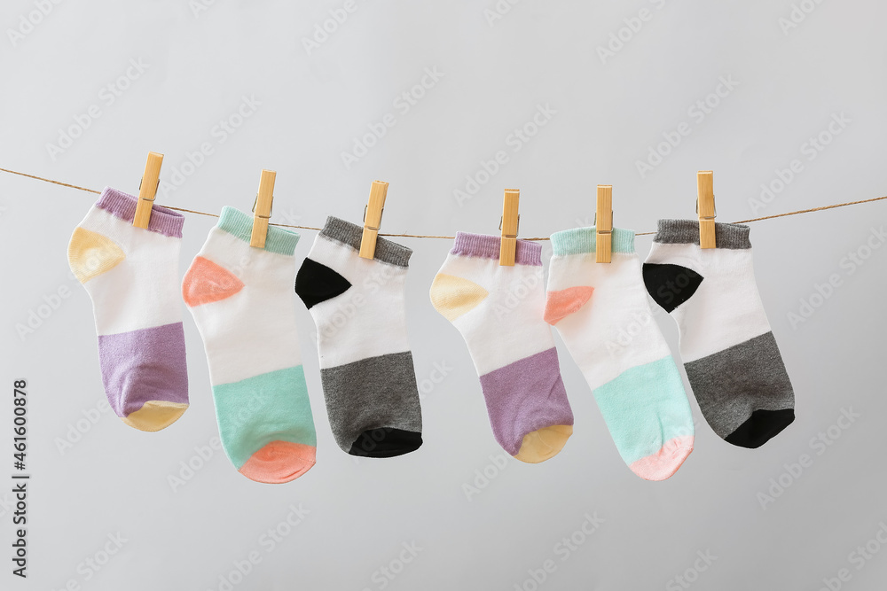 Many different socks hanging on rope against grey background