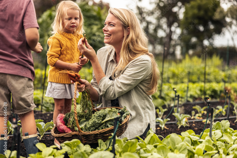 Smiling mother showing her kids a fresh carrot during harvest