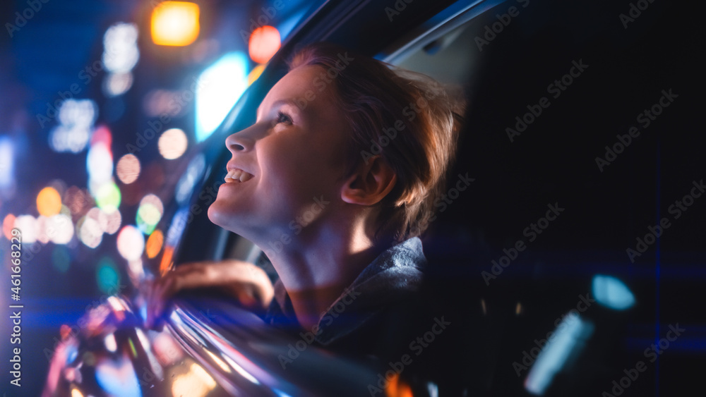 Excited Young Boy is Sitting on Backseat of a Car, Commuting Home at Night. Looking Out of the Windo