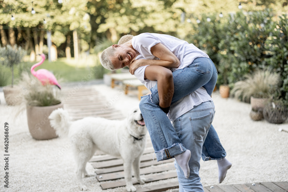 Latin boyfriend giving piggyback ride for his caucasian girlfriend on home terrace with a dog on the