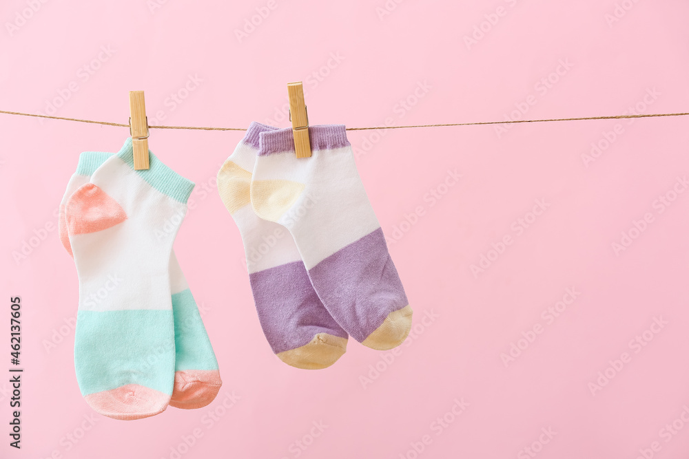 Different socks hanging on rope against pink background