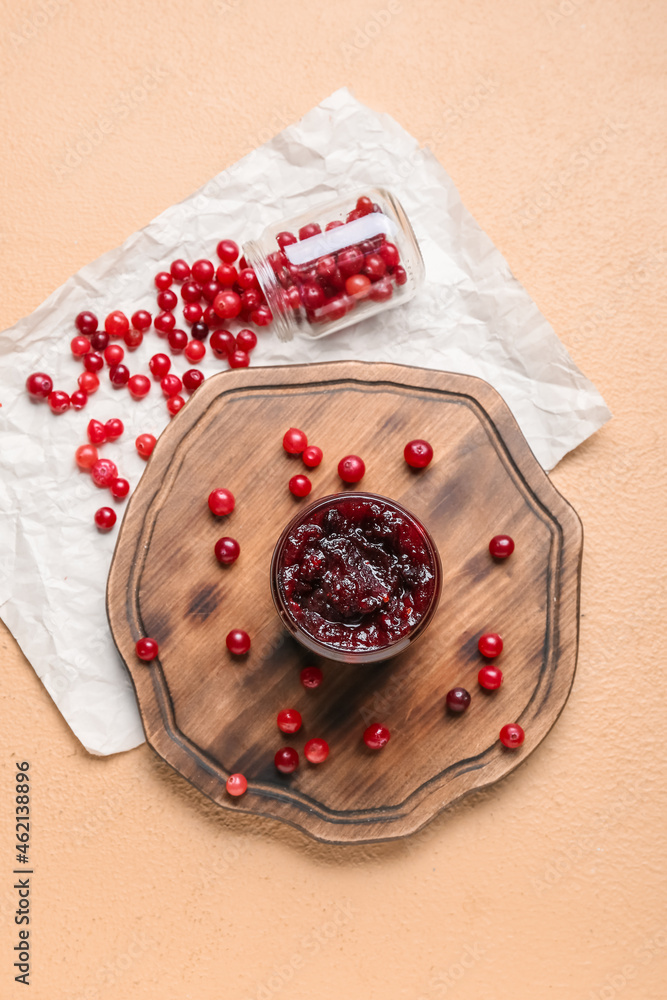 Wooden board with tasty cranberry jam and berries on color background