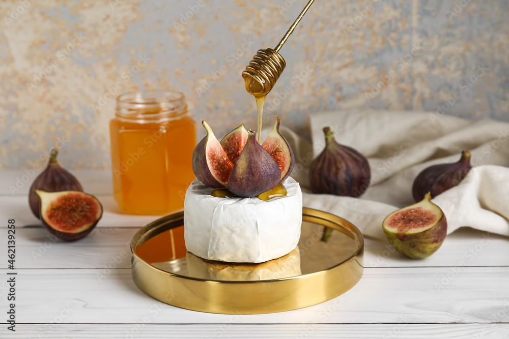 Pouring honey from dipper onto cut figs and cheese on table