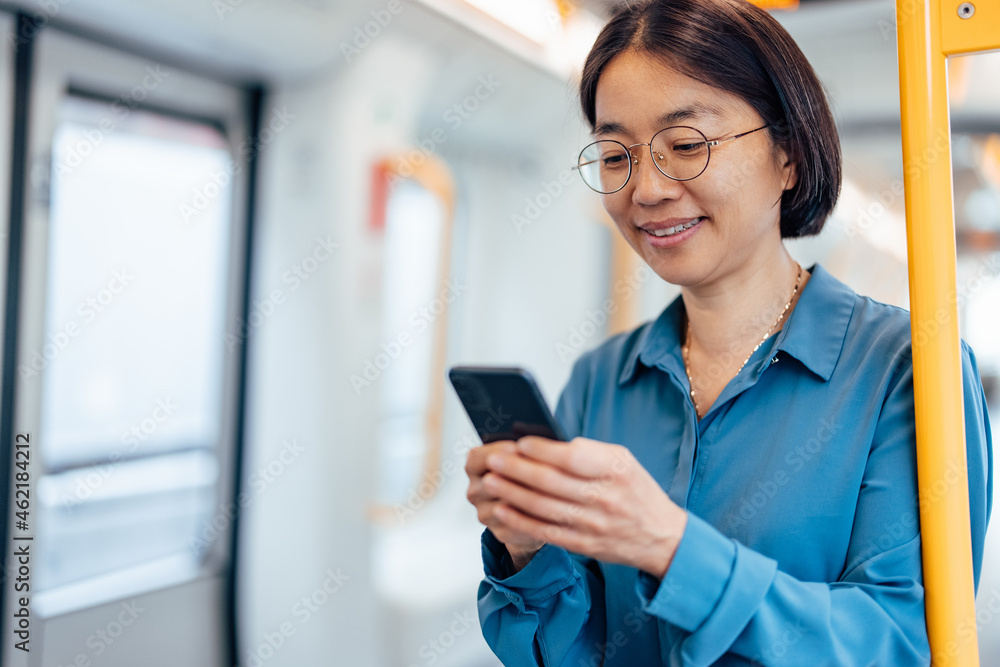 Smiling woman text messaging on smart phone while traveling by public transport.