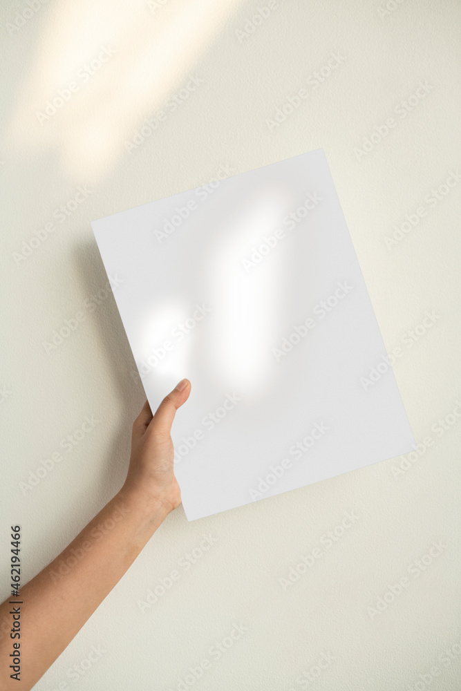 Hand holding a sheet of paper against the green wall