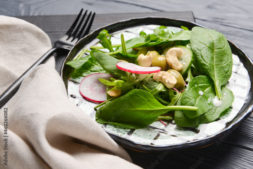 Plate with healthy salad and cashew on dark wooden background