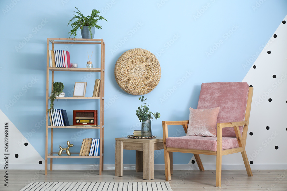 Vase with eucalyptus branches on table, armchair and bookcase near color wall