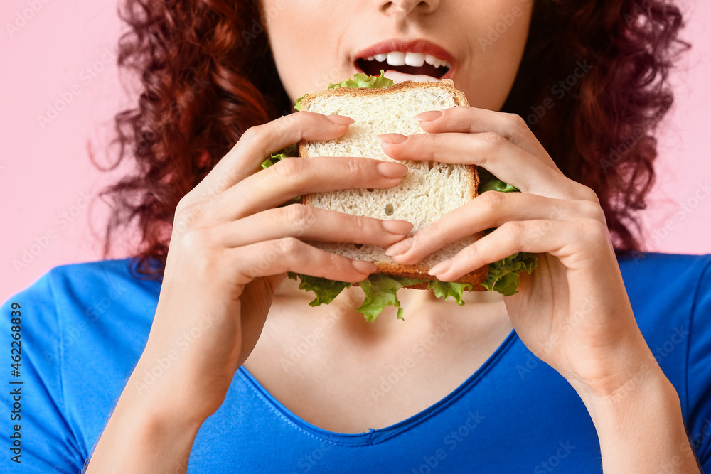 Young woman eating tasty sandwich on pink background, closeup