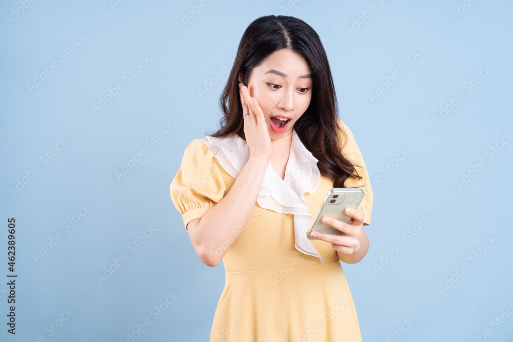 Beautiful young Asian woman using smartphone on blue background