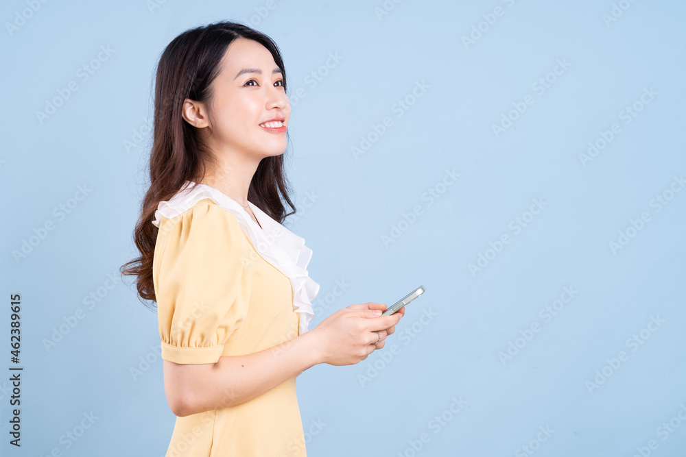 Beautiful young Asian woman using smartphone on blue background