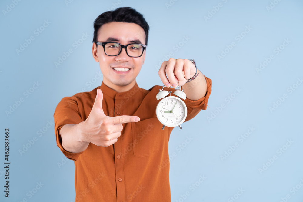 Young Asian man holding clock on blue background