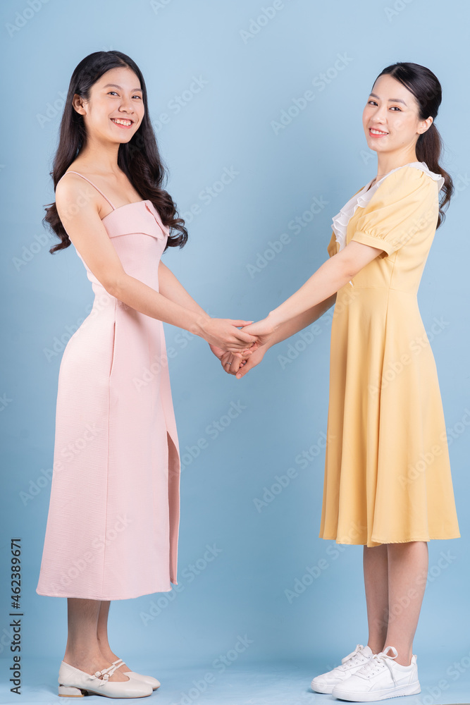 Two young Asian women wearing dress on blue background