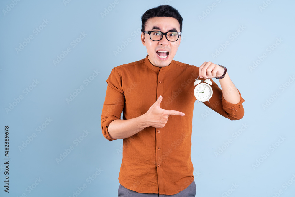 Young Asian man holding clock on blue background