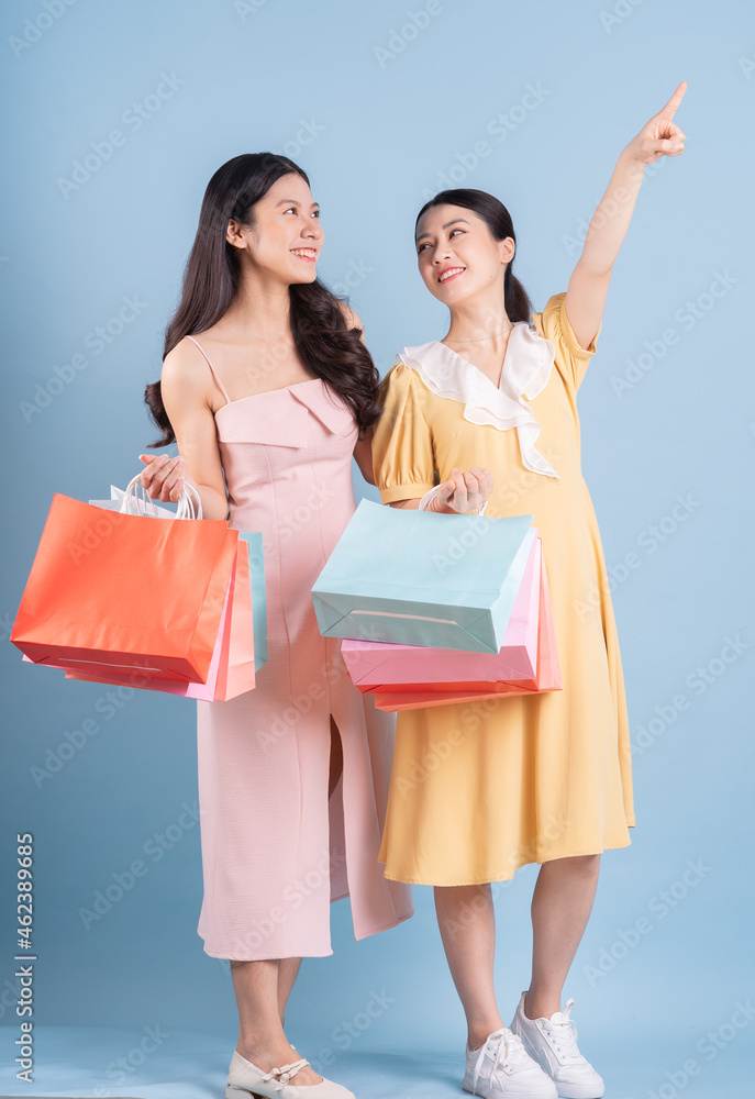 Two young Asian women holding shopping bag on blue background