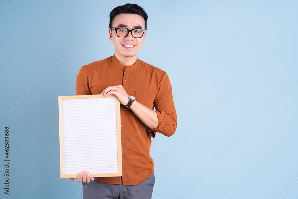 Young Asian man holding white board on blue background