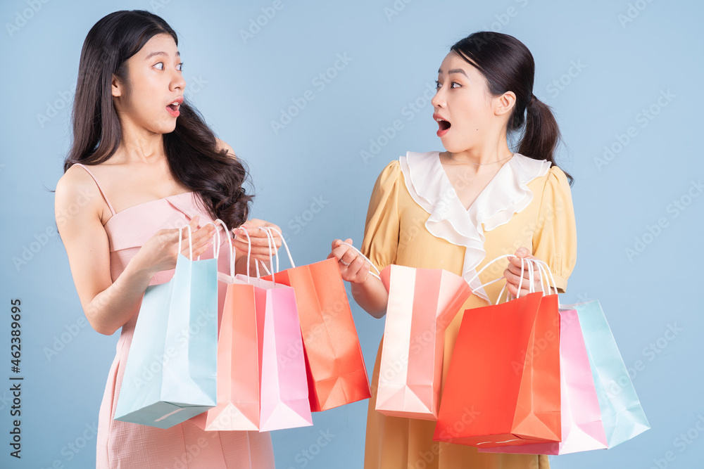 Two young Asian women holding shopping bag on blue background